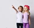 Little positive blond baby girl and boy in stylish clothing standing, hugging each other and pointing at something above Royalty Free Stock Photo