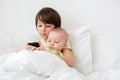 Little preschool boy laying in bed with his baby brother, playing on phone Royalty Free Stock Photo