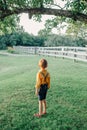 Little preschool Caucasian boy in yellow shirt and jeans shorts with suspenders standing alone in park country-side village Royalty Free Stock Photo