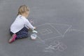 Little preschool caucasian girl drawing a house with chalks