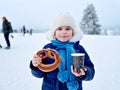 Little preschool girl drinking hot chocolate and eating pretzel in winter forest. Happy healthy child with cup of Royalty Free Stock Photo