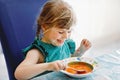 Little preschool girl eating healthy vegetable tomato soup for lunch. Cute happy child taking food at home or nursery Royalty Free Stock Photo