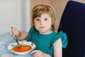 Little preschool girl eating healthy vegetable tomato soup for lunch. Cute happy child taking food at home or nursery Royalty Free Stock Photo