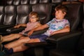 Little preschool girl with glasses and kid boy watching cartoon movie in cinema and eating popcorn. Happy excited Royalty Free Stock Photo