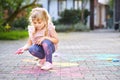 Little preschool girl painting with colorful chalks flowers on ground on backyard. Positive happy toddler child drawing Royalty Free Stock Photo