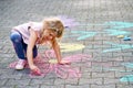 Little preschool girl painting with colorful chalks flowers on ground on backyard. Positive happy toddler child drawing Royalty Free Stock Photo