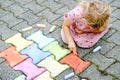 Little preschool girl painting with colorful chalks on ground on backyard. Positive happy toddler child drawing and Royalty Free Stock Photo