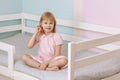 A little preschool girl in a pink dress sits on the bed combing her hair. Royalty Free Stock Photo