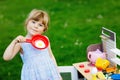Little preschool girl playing with toy kitchen in garden. Happy toddler child having fun with role activity game Royalty Free Stock Photo