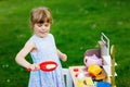 Little preschool girl playing with toy kitchen in garden. Happy toddler child having fun with role activity game Royalty Free Stock Photo