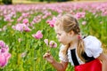 Little preschool girl in poppy field. Cute happy child in red riding hood dress play outdoor on blossom flowering meadow Royalty Free Stock Photo