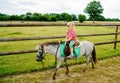 Little preschool girl riding a pony on a farm. Happy lovely child practicing horseback riding. Outdoor summer activities Royalty Free Stock Photo