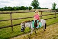 Little preschool girl riding a pony on a farm. Happy lovely child practicing horseback riding. Outdoor summer activities for Royalty Free Stock Photo