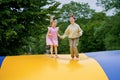 Little preschool girl and school sister jumping on trampoline. Happy funny children, siblings in love having fun with outdoor