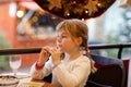 Little preschool girl sitting in restaurant near window decorated for Christmas. Child waiting for food. Happy family Royalty Free Stock Photo