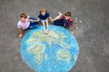 Little preschool girl and two school kids boys with earth globe painting with colorful chalks on ground. Happy earth day