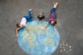 Little preschool girl and two school kids boys with earth globe painting with colorful chalks on ground. Happy earth day