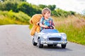 Little preschool kid boy driving big toy car and having fun with playing with his plush toy bear, outdoors. Child Royalty Free Stock Photo