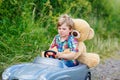 Little kid boy driving big toy car with a bear, outdoors. Royalty Free Stock Photo