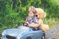 Little preschool kid boy driving big toy car and having fun with playing with his plush toy bear, outdoors. Child Royalty Free Stock Photo