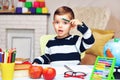 A little preschooler boy is bored and he sits at a table with a book, a globe, a notebook and pencils