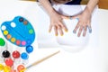 A little preschooler is sitting at a table, drawing with his palms on a sheet of paper. Colorful handprints. Preschooler