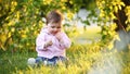 Little pretty baby-girl sitting on green grass in the park at the sunsat.