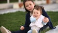 Little pretty baby-girl sitting on green grass in the park at the sunsat.