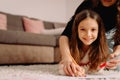 Little pretty blond girl smiling together with her mother at home drawing on the papre using red pencil, family time