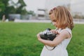 Little pretty child baby girl in light dress holding retro vintage photo camera on green grass in city park. Mother Royalty Free Stock Photo