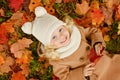 Little pretty girl in a beige coat lying on the leaves in autumn