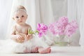 Little pretty girl with blue eyes sits on a floor with flowers of a peony. Copy space Royalty Free Stock Photo