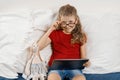 Little pretty girl in glasses sitting at home in bed with toy and digital tablet, rest and education at home. Smiling child Royalty Free Stock Photo