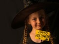 Little pretty girl witch in black wizard hat holds greeting Happy Halloween card smiling. Autumn kids party celebration Royalty Free Stock Photo