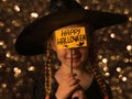 Little pretty girl witch in black wizard hat holds greeting Happy Halloween card smiling. Autumn kids party celebration Royalty Free Stock Photo