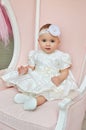 Portrait of Beatiful babygirl in white dress on pink chair in the studio. Cute kids.