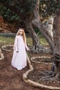 A little princess of spirits and fairies stands in the enchanted mysterious magic forest in a wedding dress with a veil and crown