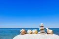 Little pyramid of white pebbles and exotic seashells on the beach on the background of the summer sea and blue sky Royalty Free Stock Photo