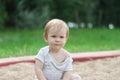 A little quiet girl sits in a sandbox on the sand