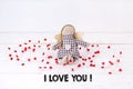 Little puppet with red hearts sitting on a wooden white background with the text `I love you`