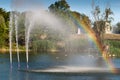 Little rainbow from the water fountain lake, city park pond, water jet beats up against the background of green trees Royalty Free Stock Photo