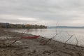 A little red boat on a lake shore near some skeletal trees, on a moody day