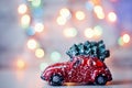 Little red car toy carrying Christmas tree in snow and bokeh christmas lights Royalty Free Stock Photo
