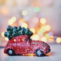 Little red car toy carrying Christmas tree in snow and bokeh christmas lights Royalty Free Stock Photo