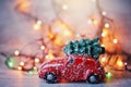 Little red car toy carrying Christmas tree in snow and bokeh christmas lights Royalty Free Stock Photo