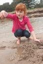 Little red haired girl building a sand castle with wet sand at a Royalty Free Stock Photo