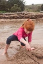 Little red haired girl building a sand castle with wet sand at a Royalty Free Stock Photo