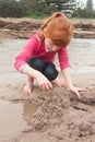 Little red haired girl building a sand castle with wet sand at a Royalty Free Stock Photo