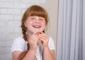 Little red-haired girl in a white dress holds a plate in her hands to correct a bite of teeth