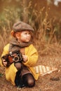 A little red-haired girl in a yellow coat and a cap with a vintage camera looking for clues on a chessboard